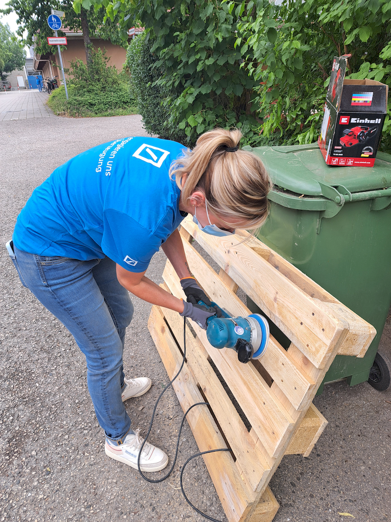 Frau schleift Holzpalette mit Schleifgerät