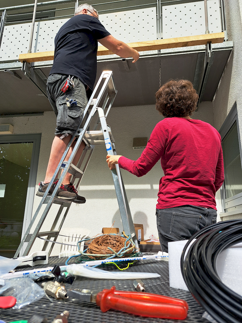 Mann steht auf Leiter und hält Balken, Frau hält die Leiter