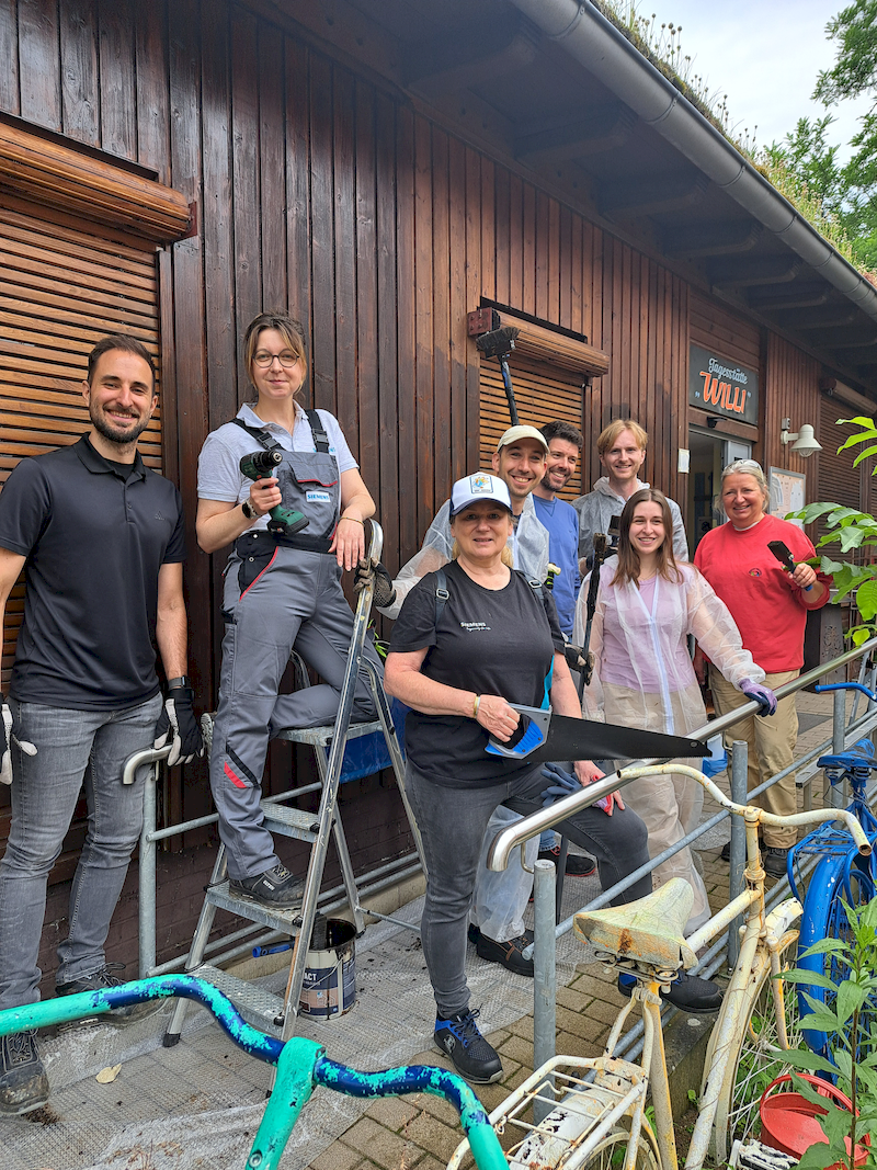 Team mit Streichutensilien steht vor Holzhaus