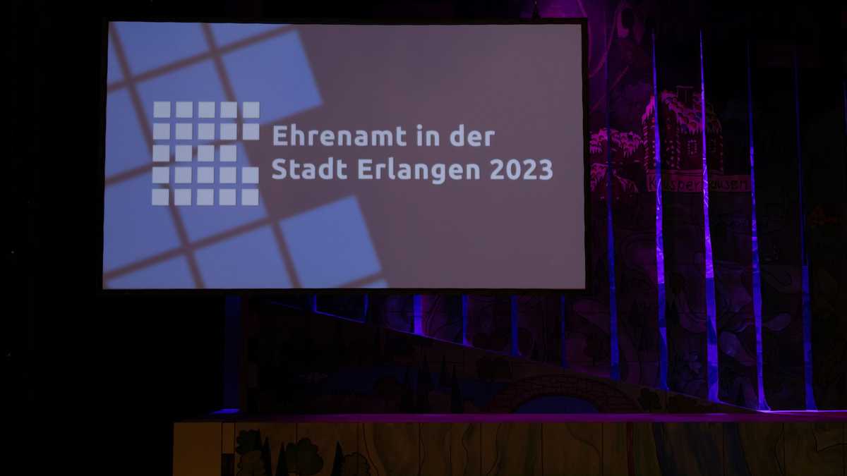 Dunkle Bühne mit Leinwand, auf der "Ehrenamt in der Stadt Erlangen 2023" steht