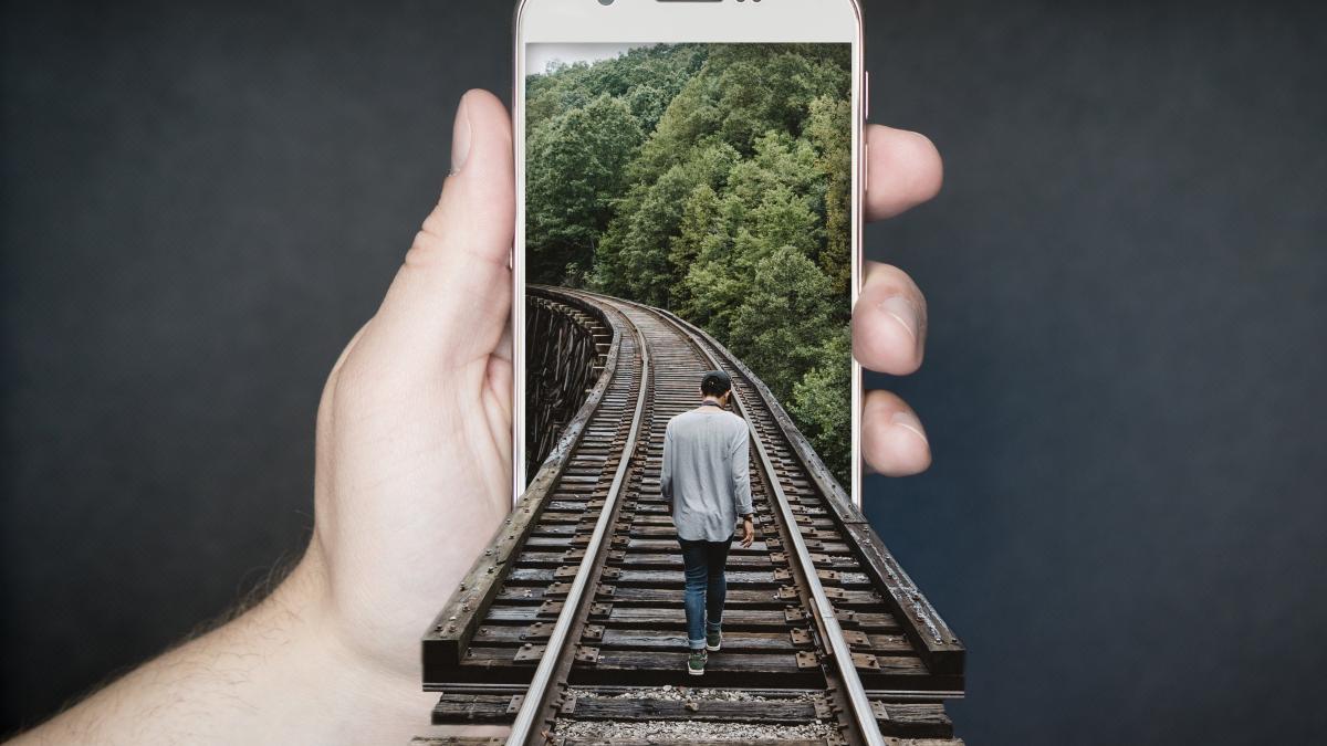 Mann läuft auf Gleisen in ein Smartphone