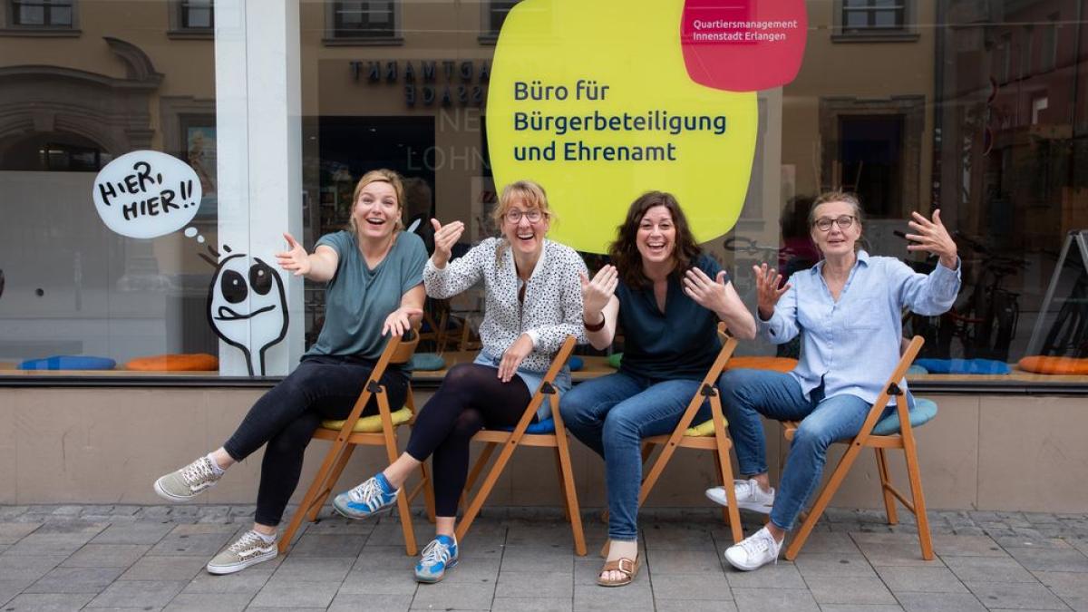 vier Frauen sitzen vor Schaufenster und winken her