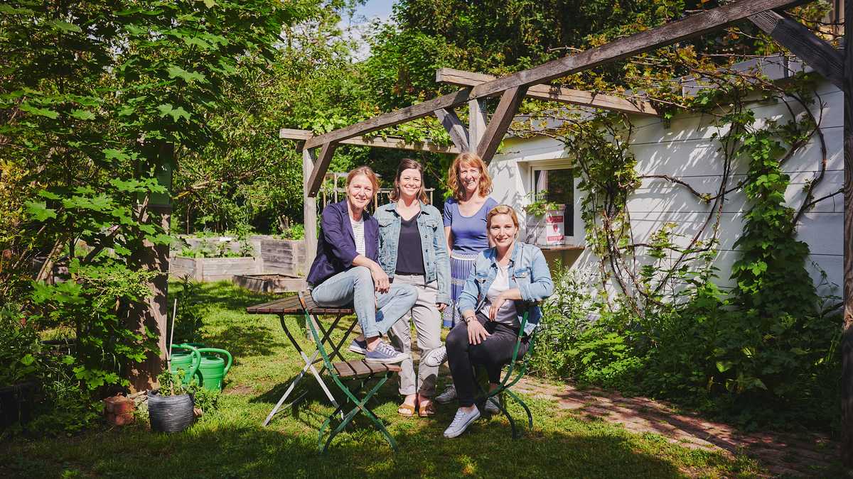 vier Frauen stehen oder sitzen auf Gartenmöbeln