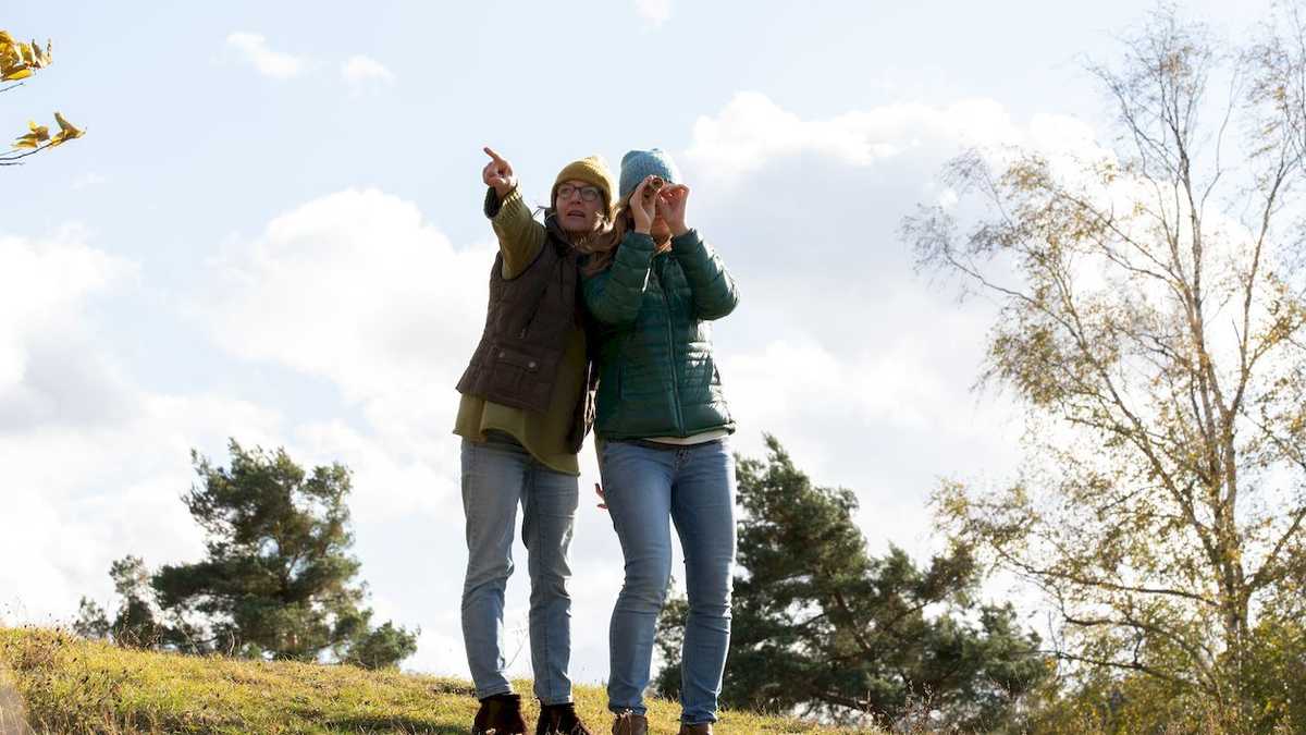 zwei Frauen stehen auf einem Hügel, eine zeigt, eine schaut durchs Fernrohr