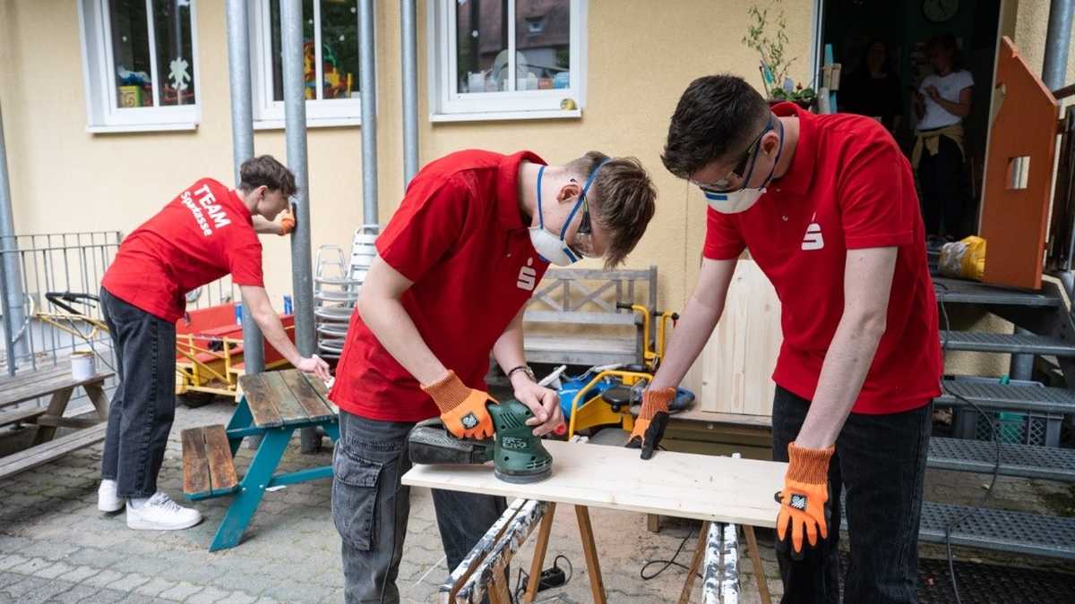 drei Männer in roten T-Shirts streichen und sägen Holz